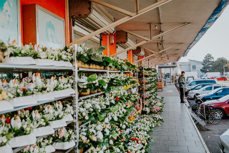 A floral display outside a flower shop along Station Road Highams Park, showcasing an array of fresh flowers arranged on tiered metal shelves under a beige awning. The flowers include white, pink, and