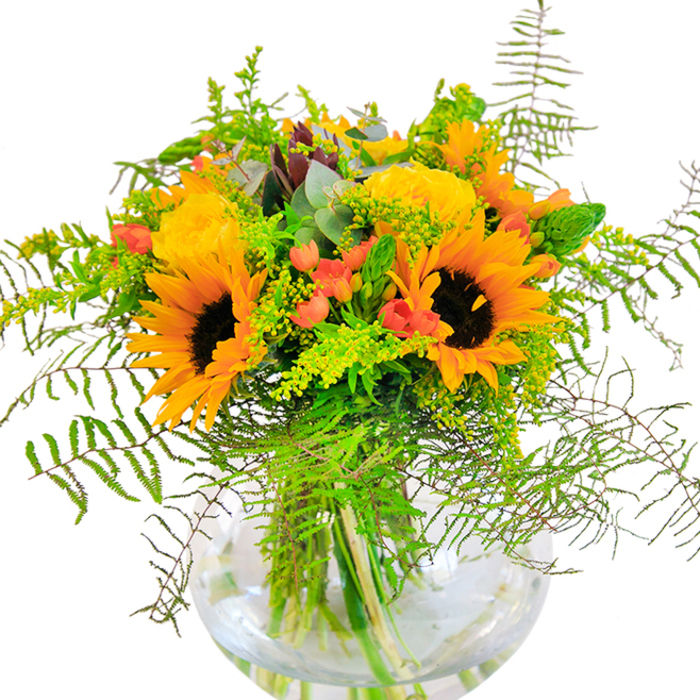 The initial impression of this stunning bouquet is one of pure sunshine, expertly arranged by florists in the heart of Highams Park to mirror the season's peak. Majestic sunflowers with bold, dark centers and exuberant yellow-orange petals stand tall, radiating optimism and brightness. Beside them bloom clusters of yellow garden roses, their velvety petals unfurling in rich layers, a promise of warmth and enduring elegance. Scarlet Hypericum berries glimmer amidst the foliage, their vivid color heightening the bouquet's vibrancy and drawing the gaze. Flowing greenery envelopes the arrangement-cascades of light, feathery fern fronds reminiscent of natural growth found along the banks of Highams Park Lake, and fluffy tufts of goldenrod or solidago graced with tiny yellow blossoms add both volume and subtle color. Sprigs of eucalyptus, tinged a serene blue-green, peek through for added texture and tranquility. The bouquet is cradled within a clear, spherical glass vase, gracefully displaying every stem and highlighting the bouquet's architectural structure; the balance of submerged stems and sparkling water accentuates the arrangement's freshness. Set against a crisp white backdrop and bathed in gentle local light, the flowers emit a soft luminosity, invoking feelings of joy and gratitude. The subtle, sweet fragrance of the roses blends with earthy greenery and faint eucalyptus, completing the multisensory experience. Whether as a centerpiece for an anniversary, a cheerful birthday gift, or a way to brighten a living room overlooking Highams Park's bustling avenues, this bouquet promises a heartfelt celebration of natural beauty and community joy.